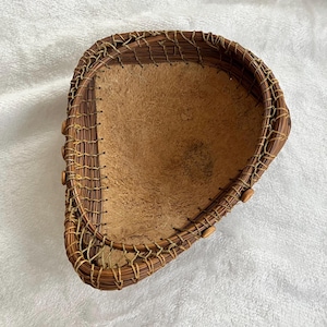 May include: Handmade brown woven basket with a light brown interior. The basket is oval-shaped with a textured surface and decorative wooden beads along the edge. The basket is made of natural materials.