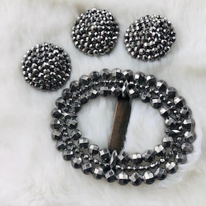 May include: A silver metal buckle with a circular design made of small, faceted beads. Three smaller circular embellishments with the same design are also included.