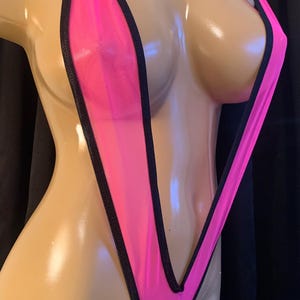 May include: A neon pink swimsuit with black trim. The swimsuit is a thong style with a halter top and a deep V-neckline. The fabric appears to be a sheer mesh material.