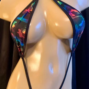 May include: A black bikini with a halter top and thong bottom. The fabric features a colorful, abstract pattern with shades of blue, pink, green, and orange. The edges are trimmed with black fabric.