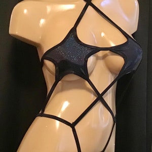May include: A black, glittery bodysuit with a halter neck and cut-out star shapes. The garment features a thong back and crisscross straps across the torso. The bodysuit is displayed on a mannequin.