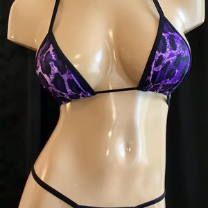 May include: Purple and black leopard print bikini set. The triangle top has halter straps and the bottoms are a thong style. The bikini is displayed on a mannequin against a black background.