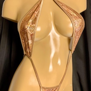 Peut inclure: Un maillot de bain doré à motif peau de serpent, avec un haut dos nu et un bas en string. Le maillot de bain est présenté sur un mannequin sur fond noir. Le tissu a un aspect chatoyant et texturé.