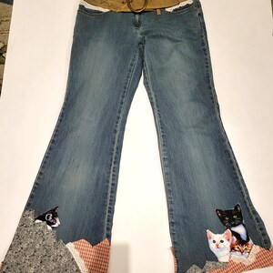 Peut inclure: Jean bleu avec une coupe évasée et une ceinture en daim marron avec une grosse boucle. Le jean est orné d'appliqués de chats sur les ourlets évasés, avec un patchwork gris, à carreaux rouges et de la dentelle.