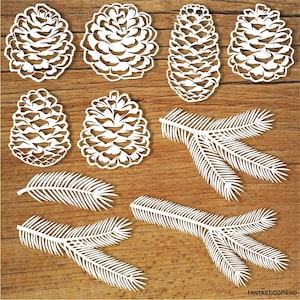 Może przedstawiać: Białe wycinanki z papieru przedstawiające szyszki i gałęzie. Szyszki są szczegółowe i realistyczne, z fakturowaną powierzchnią. Gałęzie są proste i eleganckie, o delikatnym wzorze.