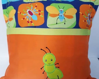 Pode incluir: Uma bolsa de tecido quadrada com duas alças e uma estampa colorida de insetos. A seção superior exibe aranhas e insetos alados em um fundo azul, enquanto a seção inferior laranja apresenta uma aplicação de uma única formiga verde.