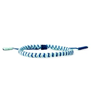 May include: A blue and white braided bracelet with adjustable ties. The bracelet features alternating stripes of light blue, dark blue, and white. The ties are a darker blue and light green. This handmade bracelet is a stylish accessory.