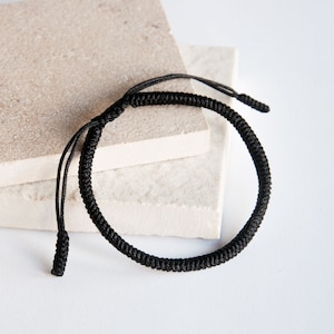 May include: A black braided bracelet with a knotted design. The bracelet is made of a thick, durable cord.