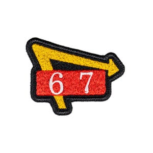 May include: Embroidered patch featuring a yellow arrow and a red rectangle with the numbers "67" in white. The patch has a black border and is likely for clothing or accessories.
