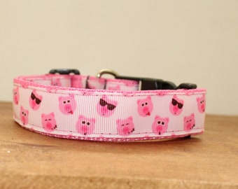 May include: A pink dog collar with a white background and a repeating pattern of pink pigs wearing sunglasses.
