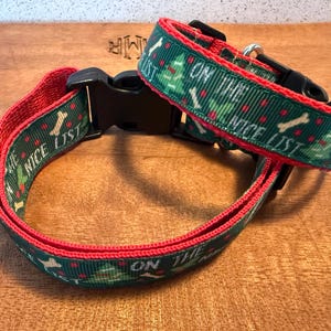 Puede incluir: Un collar verde para perros con ribete rojo y las palabras "ON THE NICE LIST". El collar presenta un patr&oacute;n de huesos blancos y &aacute;rboles de Navidad. El collar tiene una hebilla de pl&aacute;stico negro.