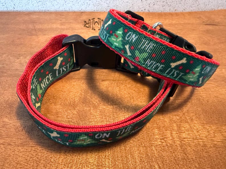 Puede incluir: Un collar verde para perros con ribete rojo y las palabras "ON THE NICE LIST". El collar presenta un patr&oacute;n de huesos blancos y &aacute;rboles de Navidad. El collar tiene una hebilla de pl&aacute;stico negro.
