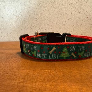 Puede incluir: Un collar festivo para perros con fondo verde, ribete rojo y hebilla negra. El collar presenta un patr&oacute;n repetido de &aacute;rboles de Navidad, huesos y el texto "ON THE NICE LIST".