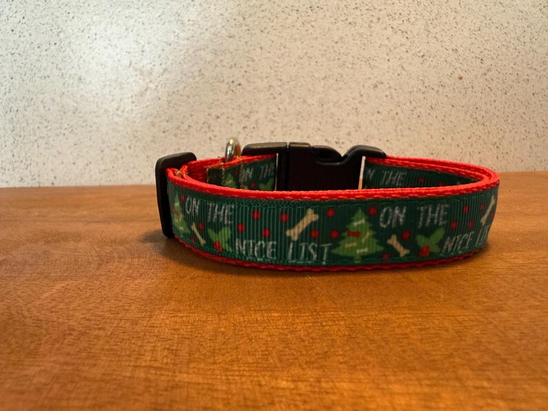 Puede incluir: Un collar festivo para perros con fondo verde, ribete rojo y hebilla negra. El collar presenta un patr&oacute;n repetido de &aacute;rboles de Navidad, huesos y el texto "ON THE NICE LIST".