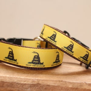 May include: Two yellow dog collars with a brown border and a repeating pattern of the Gadsden Flag, which features a coiled rattlesnake with the words "Don't Tread on Me".