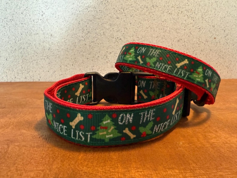 Puede incluir: Dos collares para perros con un dise&ntilde;o festivo. Los collares son verdes con ribete rojo y presentan el texto "ON THE NICE LIST", junto con im&aacute;genes de &aacute;rboles de Navidad, huesos y bayas de acebo. Se ve una hebilla de pl&aacute;stico negro.