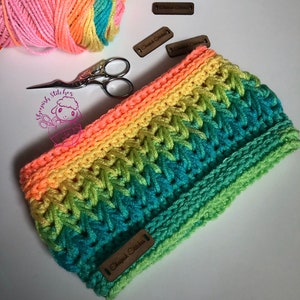 May include: A rainbow crochet headband with a textured stitch pattern. The headband is made with a variety of colors, including pink, orange, yellow, green, and blue. The headband is labeled with a brown tag that says "Sheepish Stitches".