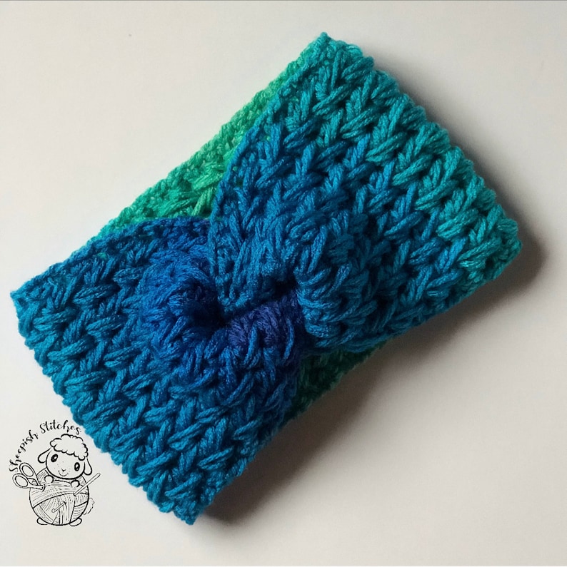 May include: A blue and green crocheted headband with a knotted design. The headband is made with a soft yarn and has a comfortable fit.