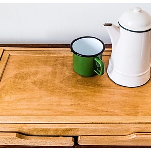 May include: A wooden serving tray with two drawers, a green enamel mug, and a white enamel teapot with a black rim and green handle.