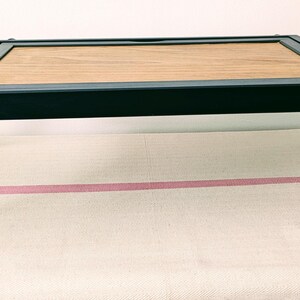 May include: A black wooden folding tray with a rectangular wooden top. The tray is folded and sitting on a white surface.