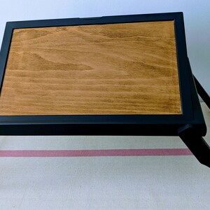 May include: A black wooden folding tray with a brown wood top. The tray is folded and sitting on a white and pink striped surface.