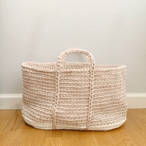 Może przedstawiać: Duża, dziana torba typu tote w jasnoróżowym kolorze z białym wykończeniem u dołu. Torba ma dwa grube uchwyty.