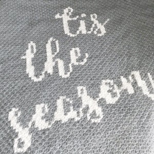 K&ouml;nnte beinhalten: Graue Wurfdecke mit wei&szlig;em Text, der "Tis the season" lautet.