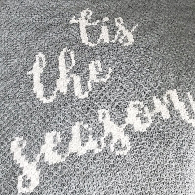 K&ouml;nnte beinhalten: Graue Wurfdecke mit wei&szlig;em Text, der "Tis the season" lautet.