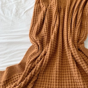 May include: A brown waffle knit throw blanket folded on a white bedspread.