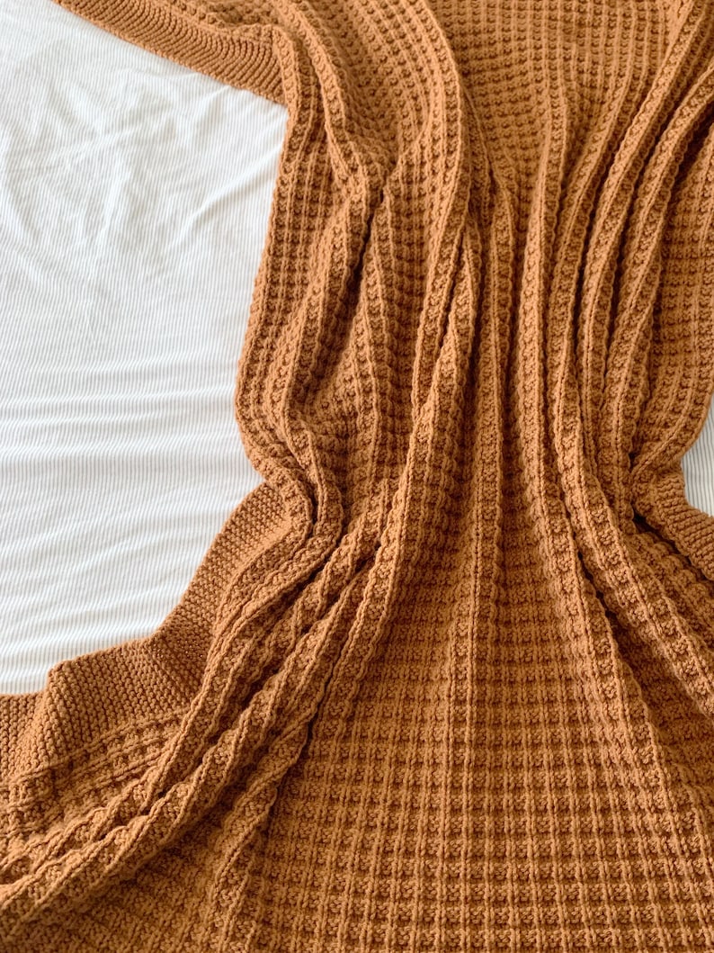 May include: A brown waffle knit throw blanket folded on a white bedspread.