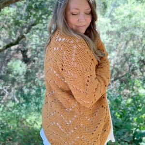 May include: A mustard yellow crocheted cardigan with a lacy pattern. The cardigan is worn over a white shirt and blue jeans.