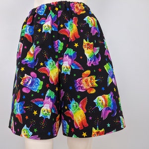 K&ouml;nnte beinhalten: Schwarze Shorts mit elastischem Bund, bedeckt mit einem bunten Muster aus gefl&uuml;gelten Katzen mit Einhorn-H&ouml;rnern und Sternen. Die Katzen haben Regenbogenfarben und sind in verschiedenen Posen.