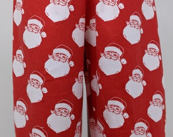 Puede incluir: Tela roja con un patrón repetido de caras blancas de Papá Noel. Las caras de Papá Noel tienen barbas blancas y gorros rojos. La tela parece ser parte de una prenda, posiblemente un pijama o pantalón.