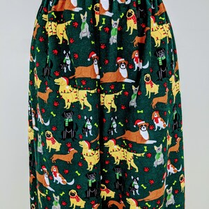 May include: Green pajama pants with an all-over pattern of various dog breeds wearing holiday accessories. The dogs are in brown, yellow, black, and white, with red paw prints and bone accents. The pants have an elastic waistband.