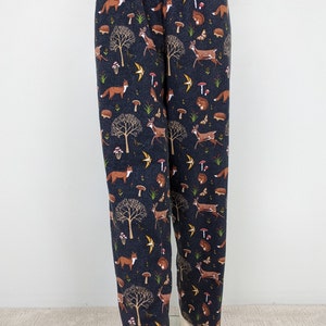 May include: Dark navy blue pajama pants with an all-over woodland pattern. The print includes foxes, deer, mushrooms, trees, and birds. The pants have an elastic waistband and a relaxed fit.
