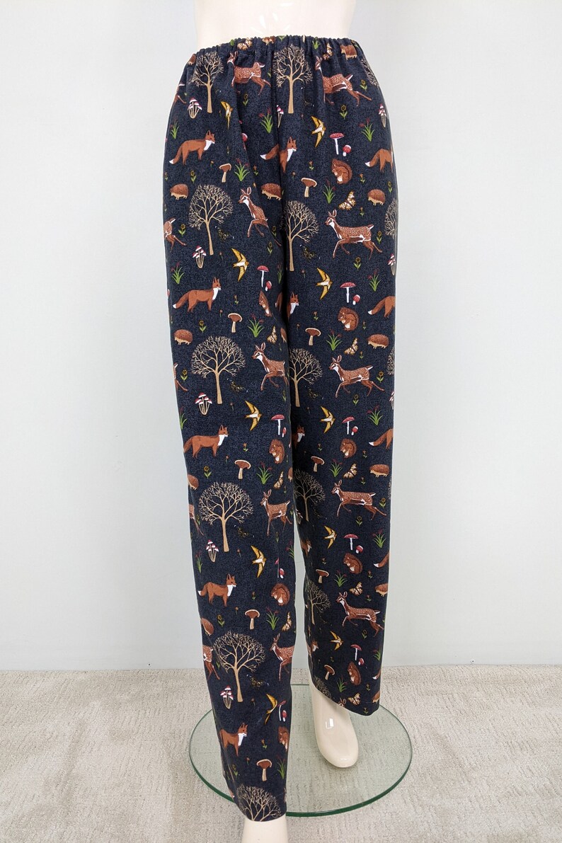 May include: Dark navy blue pajama pants with an all-over woodland pattern. The print includes foxes, deer, mushrooms, trees, and birds. The pants have an elastic waistband and a relaxed fit.