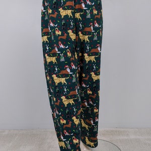 May include: Dark green pajama pants with an all-over pattern of various dog breeds wearing holiday accessories. The dogs are in shades of brown, black, and gold, with red and green accents. The pants have an elastic waistband.