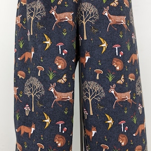 May include: Dark blue fabric with a repeating pattern of woodland creatures and elements. The design includes deer, foxes, squirrels, mushrooms, butterflies, birds, and trees. The fabric is likely used for clothing or home decor.