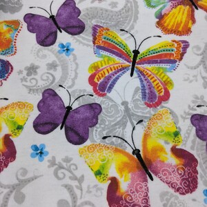 Puede incluir: Tela blanca con un patr&oacute;n repetitivo de mariposas coloridas. Las mariposas son de varios tonos de morado, amarillo, rosa y verde.