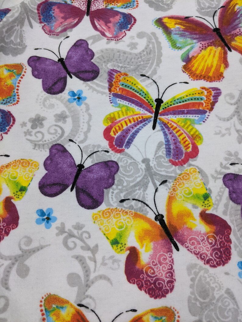 Puede incluir: Tela blanca con un patr&oacute;n repetitivo de mariposas coloridas. Las mariposas son de varios tonos de morado, amarillo, rosa y verde.
