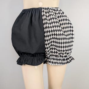 May include: Black and white harlequin-patterned bloomers. One side is solid black, the other features a diamond pattern. The elastic waistband and ruffled leg openings add a playful touch. These shorts are a unique addition to any wardrobe.