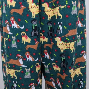 May include: Green pajama pants with a repeating pattern of various dog breeds, including dachshunds, pugs, and golden retrievers. Some dogs are wearing Santa hats, scarves, or Christmas lights. Paw prints and bones are scattered throughout the design.