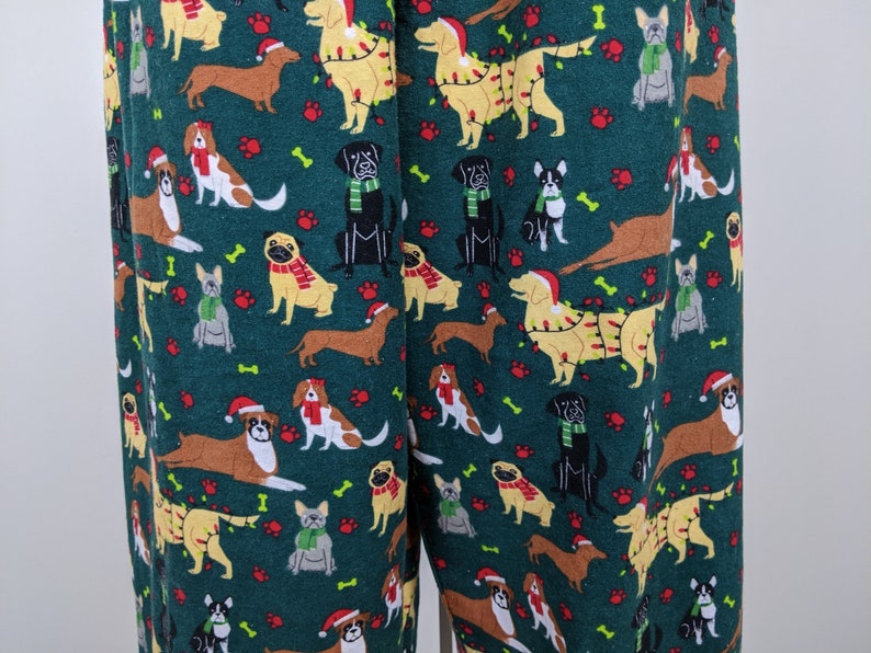 May include: Green pajama pants with a repeating pattern of various dog breeds, including dachshunds, pugs, and golden retrievers. Some dogs are wearing Santa hats, scarves, or Christmas lights. Paw prints and bones are scattered throughout the design.