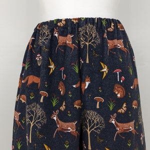 May include: Dark blue pajama pants with an elastic waistband. The fabric features a repeating pattern of woodland creatures, including deer, foxes, squirrels, and hedgehogs, along with trees, mushrooms, and butterflies. The pants are made of a soft, comfortable material.