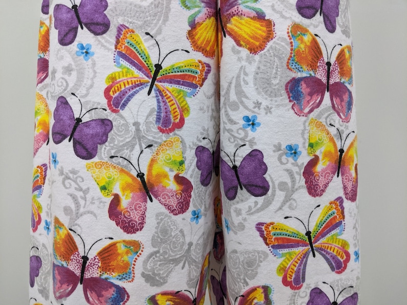 Puede incluir: Tela blanca con un patr&oacute;n repetido de mariposas coloridas. Las mariposas tienen acentos morados, amarillos, naranjas, rosados y verdes.