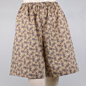 May include: Beige shorts with a pattern of gray sock monkeys. The shorts have an elastic waistband and a relaxed fit.