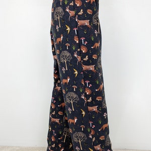 May include: Dark navy blue pajama pants with an all-over woodland print. The pattern includes brown foxes, deer, mushrooms, trees, butterflies, and hedgehogs. The pants have an elastic waistband.