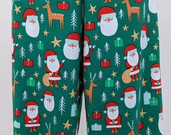 Puede incluir: Pantalones de pijama verdes con temática navideña con un patrón repetido de Papá Noel, renos, árboles de Navidad, estrellas y regalos envueltos. Las figuras de Papá Noel tienen barbas blancas y gorros rojos.