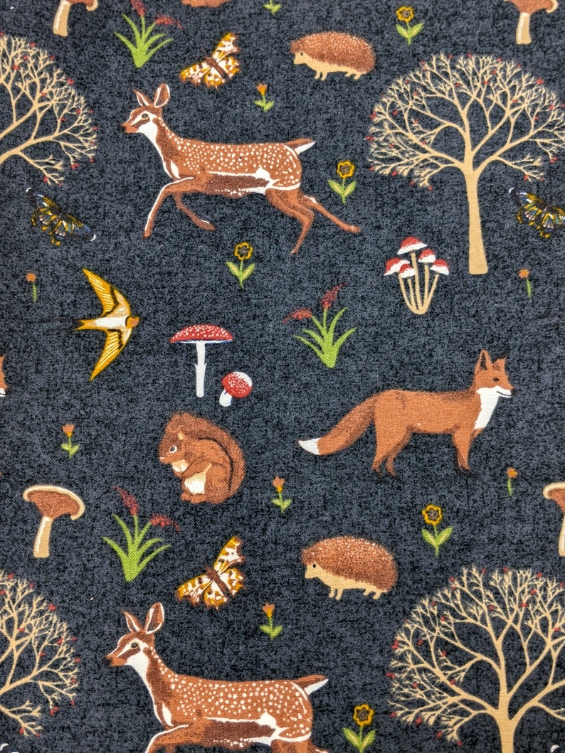 May include: A fabric with a dark gray background featuring a repeating pattern of woodland creatures and elements. The design includes deer, foxes, squirrels, butterflies, mushrooms, trees, and flowers in shades of brown, orange, yellow, and white.
