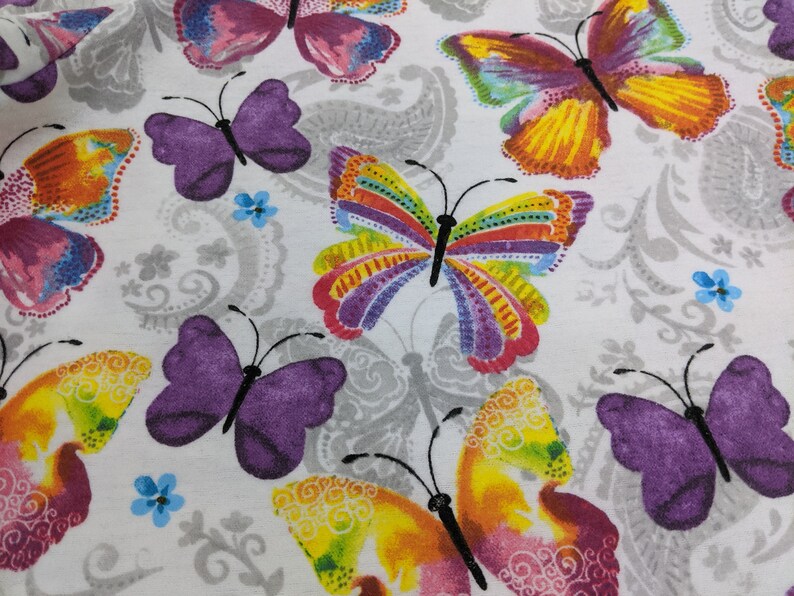 Puede incluir: Tela blanca con un patr&oacute;n repetitivo de mariposas de colores. Las mariposas tienen alas moradas, rosas, amarillas, naranjas, rojas, verdes y azules.